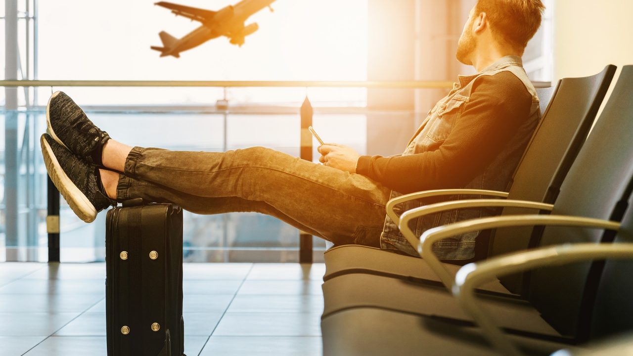 空港でスマホ片手に飛行機をみながら時間を潰す男性の手荷物（人）